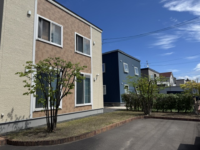 Residential street with beige and blue modern townhouses, small trees, and a paved driveway under a blue sky.